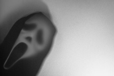 Bangkok, Tayland - 18 Ağustos 2023: Çığlık atan korku maskesinin gölgesi. Buzlu camların arkasındaki tehlikeli adam. Gizemli adam. Siyah beyaz resim. Görüntü..