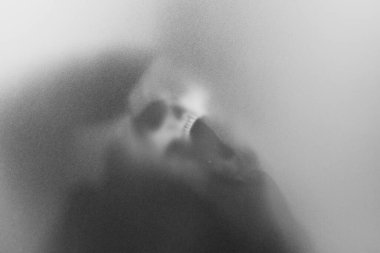 Bangkok, Tayland - 20 Ağustos 2023: gizemli bir adam elinde bir kafatası tutuyor buzlu camın arkasında duruyor gizemli ve korkutucu bir büyücü gibi görünüyor.