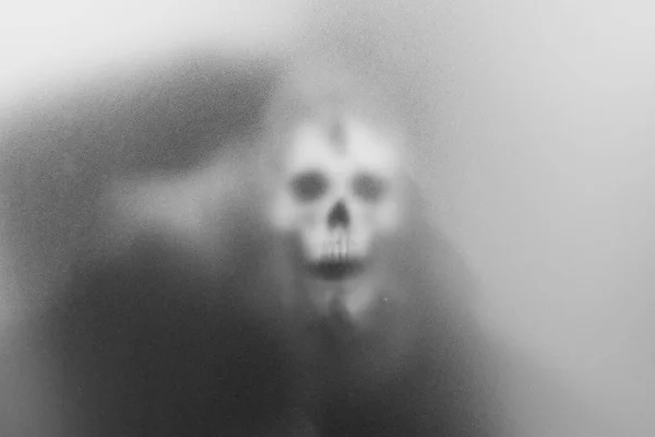 Bangkok, Thailand - August, 20, 2023 : Mysterious man holding a skull in his hand standing behind frosted glass looking mysterious and scary looking like a sorcerer.haunting concept.Halloween concept