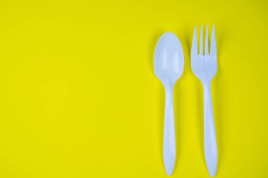 Sarı arka planda beyaz plastik kaşıklar ve çatallar.