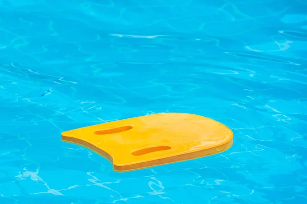 Yellow kick board made of foam floating on water surface in swimming pool.