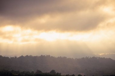 Kalın bulutları delip geçen, aşağıdaki sisli sıradağları aydınlatan güneş ışınlarının nefes kesici görüntüsü..