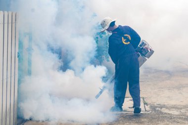 A health worker uses a fogging machine to control mosquito populations in an urban setting. clipart