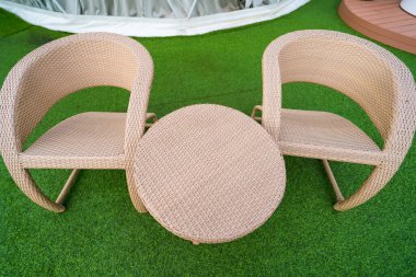 Dışarıdaki hasır kanepe ve masa seti dairesel dizaynlı, yeşil suni çimlerin üzerine yerleştirilmiş, bambu arka planı olan, rahat bir açık hava oturma alanı yaratmak için ideal..