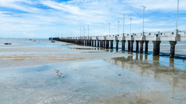 A tranquil pier extending into the sea during low tide, with reflections in the shallow water and a clear blue sky above. clipart