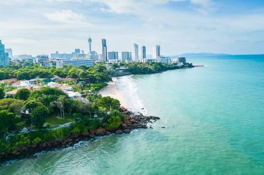 Modern gökdelenlerin ve yeşil yeşilliklerin yer aldığı bir sahil manzarası, doğal ortamda kentsel gelişimin güzelliğini yakalıyor..