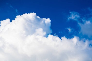 Açık mavi gökyüzünde yüzen tüylü beyaz bulutların yer aldığı barışçıl bir sahne, arka plan veya doğa temalı projeler için idealdir..