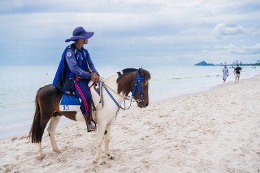 Huzurlu bir at gezisi, sakin bir plaj ve bulutlu bir gökyüzü. Görüntü, sahil şeridi boyunca sürmenin uyumunu yakalıyor..