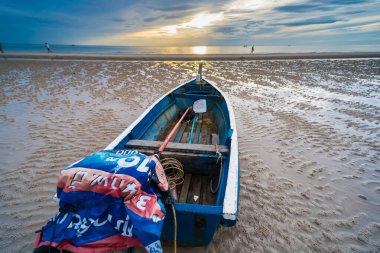 Şafakta bir balıkçı teknesi, gökyüzü mavi ve turuncu renklerle boyanmış, sabahın erken saatlerinin güzelliğini yansıtıyor..