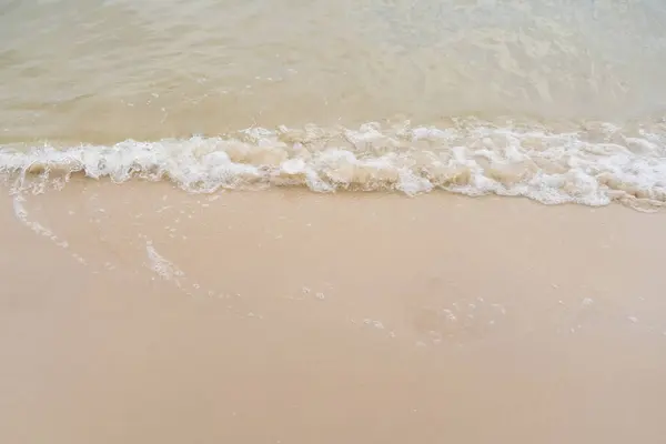 stock image Gentle waves roll onto a sandy shore, creating a peaceful and serene beach scene.