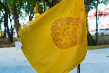 yellow Dharmachakra flag, its vibrant colors faded by time and weather. The flag is hanging limply on a flagpole, its edges frayed and torn. clipart