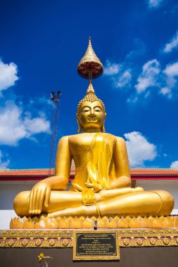 Huzurlu, altın bir Buda heykeli. Meditasyon pozu veren bir heykel. Canlı, mavi bir gökyüzünün altında, beyaz bulutlu..