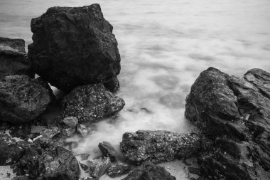 Huzurlu bir deniz manzarası. Eski kayaların nazik dalgalarla buluştuğu sonsuz bir dans. Siyah beyaz fotoğraf.