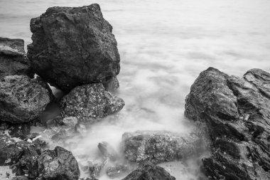 Huzurlu bir deniz manzarası. Eski kayaların nazik dalgalarla buluştuğu sonsuz bir dans. Siyah beyaz fotoğraf.