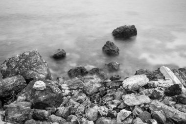 Huzurlu bir deniz manzarası. Eski kayaların nazik dalgalarla buluştuğu sonsuz bir dans. Siyah beyaz fotoğraf.