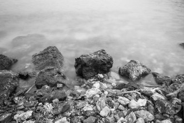 Huzurlu bir deniz manzarası. Eski kayaların nazik dalgalarla buluştuğu sonsuz bir dans. Siyah beyaz fotoğraf.