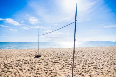 Güneşli bir plaj voleybol sahası, altın kum ve açık mavi gökyüzü, yaz eğlencesinin özünü yakalıyor..