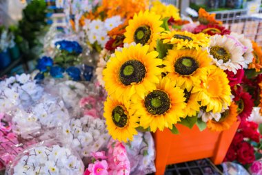 Ayçiçekleri, papatyalar ve güller de dahil olmak üzere çeşitli yapay çiçeklerin göz alıcı ve göz alıcı bir şekilde sergilenmesi..