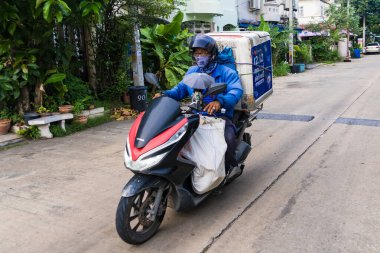 Nonthaburii, Tayland - 24 Haziran 2024: Motosikletli kurye Nonthaburii, Tayland 'da büyük konteynırları olan bir banliyö bölgesinde mal taşıyor.