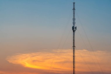 Gün batımında bir iletişim kulesinin silüeti. Renkli gökyüzüne karşı birden fazla anten ve verici içeriyor..