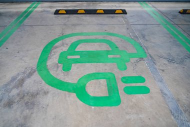 Elektrik yükleme için belirlenmiş park yeri, koyu yeşil bir sembolle işaretlenmiş, elektrikli araçların evlat edinilmesini teşvik eden.