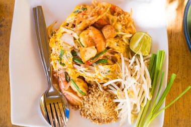 Bu canlı görüntü, içinde karides, tofu ve taze sebzelerin yer aldığı limon ve fıstıkla süslenmiş bir tabak Pad Thai tabağı gösteriyor. Yemek blogları, Tayland mutfağı makaleleri ve restoran menüleri için mükemmel..