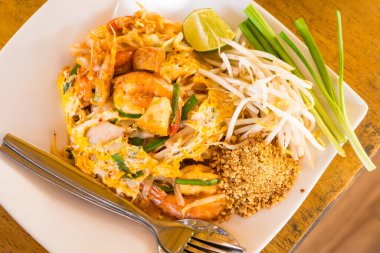 Bu canlı görüntü, içinde karides, tofu ve taze sebzelerin yer aldığı limon ve fıstıkla süslenmiş bir tabak Pad Thai tabağı gösteriyor. Yemek blogları, Tayland mutfağı makaleleri ve restoran menüleri için mükemmel..