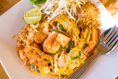 Bu canlı görüntü, içinde karides, tofu ve taze sebzelerin yer aldığı limon ve fıstıkla süslenmiş bir tabak Pad Thai tabağı gösteriyor. Yemek blogları, Tayland mutfağı makaleleri ve restoran menüleri için mükemmel..