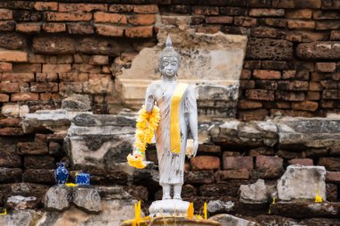 Ayutthaya, Tayland - 26 Nisan 2024: Serene Buddha figürü Ayutthaya, Tayland 'da Kırsal Tuğlaya Karşı, Sarı Garland' da Sarılı.