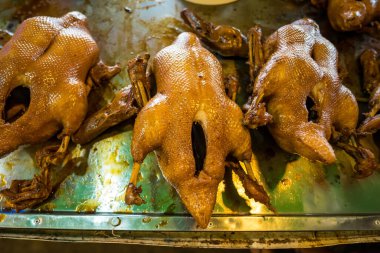 Geleneksel pazar ortamında asılı altın sarısı kavrulmuş ördekler. Mutfak geleneklerini sergilemek için mükemmel..