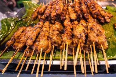 Lezzetli ızgara tavuk şişleri muz yaprağına yerleştirilmiş, Tayland sokak yemeklerinin özünü yakalıyor..