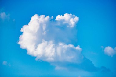 Bu büyüleyici görüntü, tüylü, beyaz bulutların zarif bir şekilde mavi gökyüzünde sürüklenip durgun ve sakinleştirici bir atmosfer oluşturduğu nefes kesici bir manzara sergiliyor..