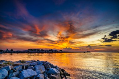 Kayalık kıyılar, sakin sular ve canlı gökyüzünün yer aldığı nefes kesici bir sahil gün batımı sahnesi..