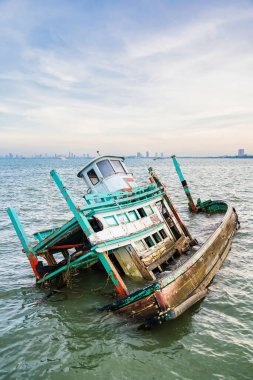 Chonburi, Thailand - November, 18, 2024 : Wooden Fishing Vessel Wreckage Partially Submerged in Water with Skyline in the Distance at Chonburi, Thailand. clipart