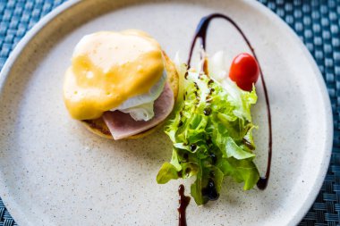 Jambonlu Benedict usulü yumurta, Hollandaise sosu ve yanında taze salata olan gurme kahvaltı tabağı..