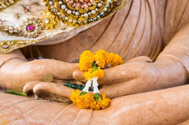Phetchabun, Thailand - January, 06, 2025 : Yellow marigold flower garland in the hands of a marble Buddha statue, symbolizing deep faith and offerings in Thai Buddhist culture  at Phetchabun, Thailand.