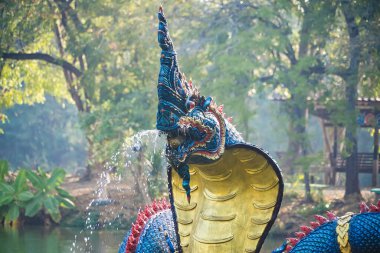Lop Buri, Tayland - Ocak 02, 2025: Lop Buri, Tayland 'da güneşli bir günde yemyeşil ağaçlarla çevrili sakin bir park gölündeki dev yılan heykeli.