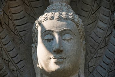Huzurlu bir Buda heykeline yakın çekim. Karmaşık oymalar ve yüzüne yansıyan hafif güneş ışığı.