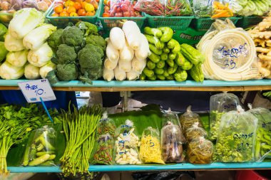Brokoli, bok çuvalı, lahana gibi taze sebzelerin ve paketli bitkilerin bulunduğu renkli bir piyasa.