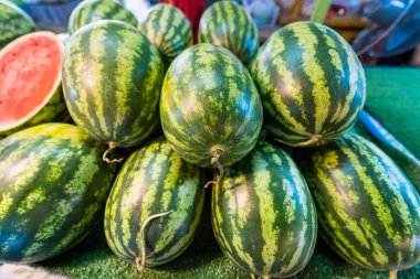 Bir market tezgahında sergilenen canlı kırmızı et ve koyu tohumları ortaya çıkarmak için tek kesikli taze bir karpuz yığını.