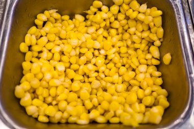 Ticari mutfak veya büfe servis tepsisinde sergilenen sarı mısır taneleriyle dolu bir konteynır.