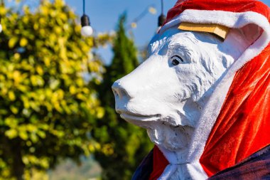 Kışın giyinmiş bir kutup ayısı heykeli. Bahçede duran kırmızı Noel Baba şapkası ve eşarbı da dahil.
