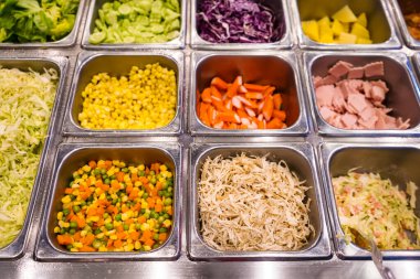 Sebze, ton balığı, mısır, havuç, mor lahana ve ananas gibi çeşitli taze malzemelerle dolu bir salata barının en üst görüntüsü.