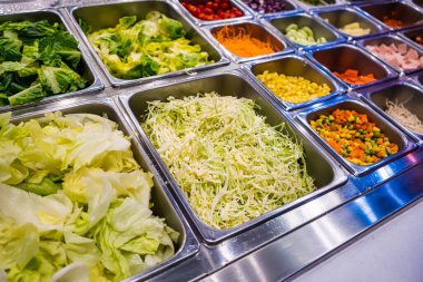 Lokanta büfesindeki paslanmaz çelik salata barında sergilenen taze sebzeler arasında marul, mısır ve doğranmış lahana da var.