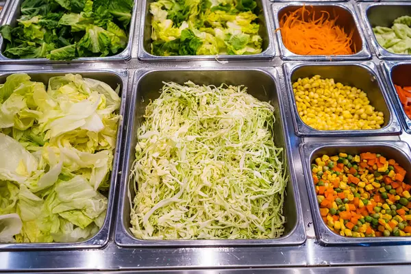 Lokanta büfesindeki paslanmaz çelik salata barında sergilenen taze sebzeler arasında marul, mısır ve doğranmış lahana da var.