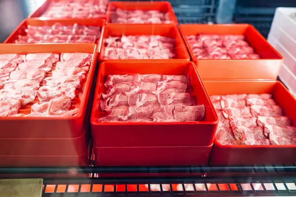 Bir süpermarkette ya da markette buzdolabında sergilenen ince dilimlenmiş etle dolu kırmızı kaplar.