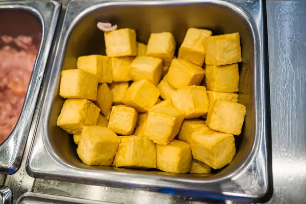 Altın sarısı, bol yağda kızartılmış tofu küpleriyle dolu paslanmaz çelik bir tepsi servis alanında sergileniyor..