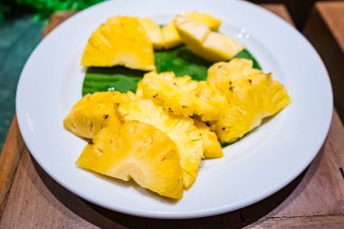 Dilimlenmiş ananas, yeşil yapraklı beyaz bir tabakta garnitür olarak servis edilir, ferahlatıcı ve tropikal bir sunum yaratır.