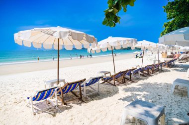 Rayong, Tayland - Nisan 01, 2025: Açık mavi gökyüzü altında sıralanmış renkli güverte sandalyeleri ve şemsiyeleri olan el değmemiş kumlu plaj, Koh Samet, Rayong, Tayland 'da okyanusun tadını çıkaran insanlar
