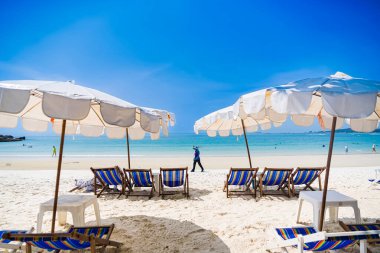 Rayong, Tayland - Nisan 01, 2025: Açık mavi gökyüzü altında sıralanmış renkli güverte sandalyeleri ve şemsiyeleri olan el değmemiş kumlu plaj, Koh Samet, Rayong, Tayland 'da okyanusun tadını çıkaran insanlar